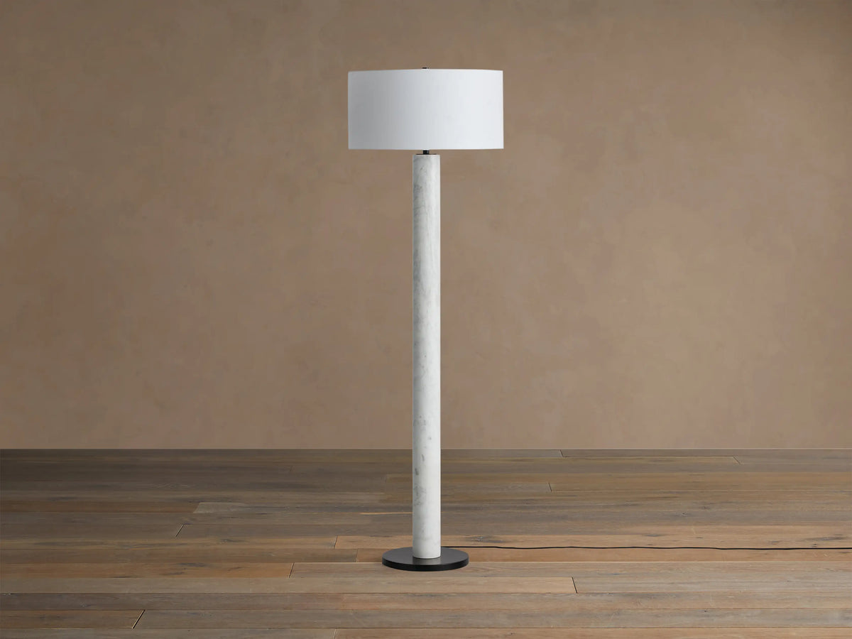 Brixton Floor Lamp: Tall white marble column, white cylindrical fabric shade, round black base. On wooden floor.