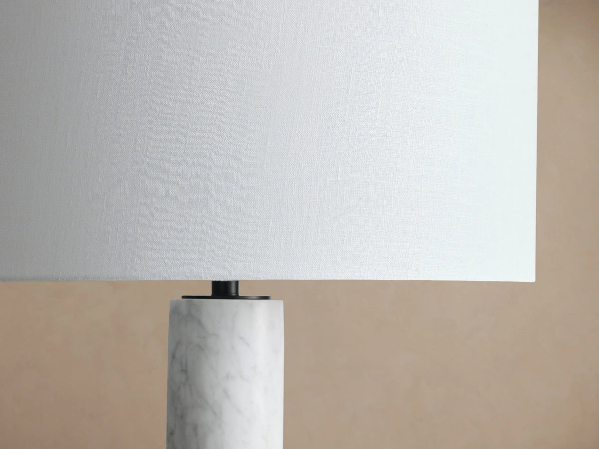 Brixton Floor Lamp with white cylindrical shade, white marble column, and dark round base on wooden floor against neutral wall.