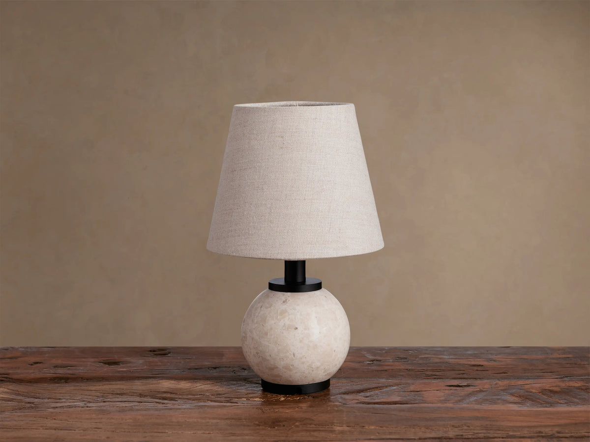 Celia Outdoor Rechargeable Lamp on rustic wood table. Cream marble base, matte black accents, lighted flax linen shade.
