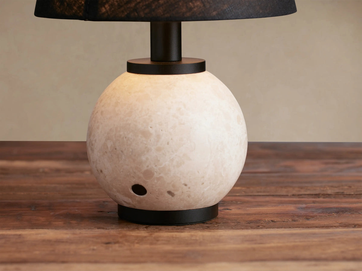 Celia Outdoor Rechargeable Lamp with creamy travertine spherical base, matte black hardware, and flax linen shade.