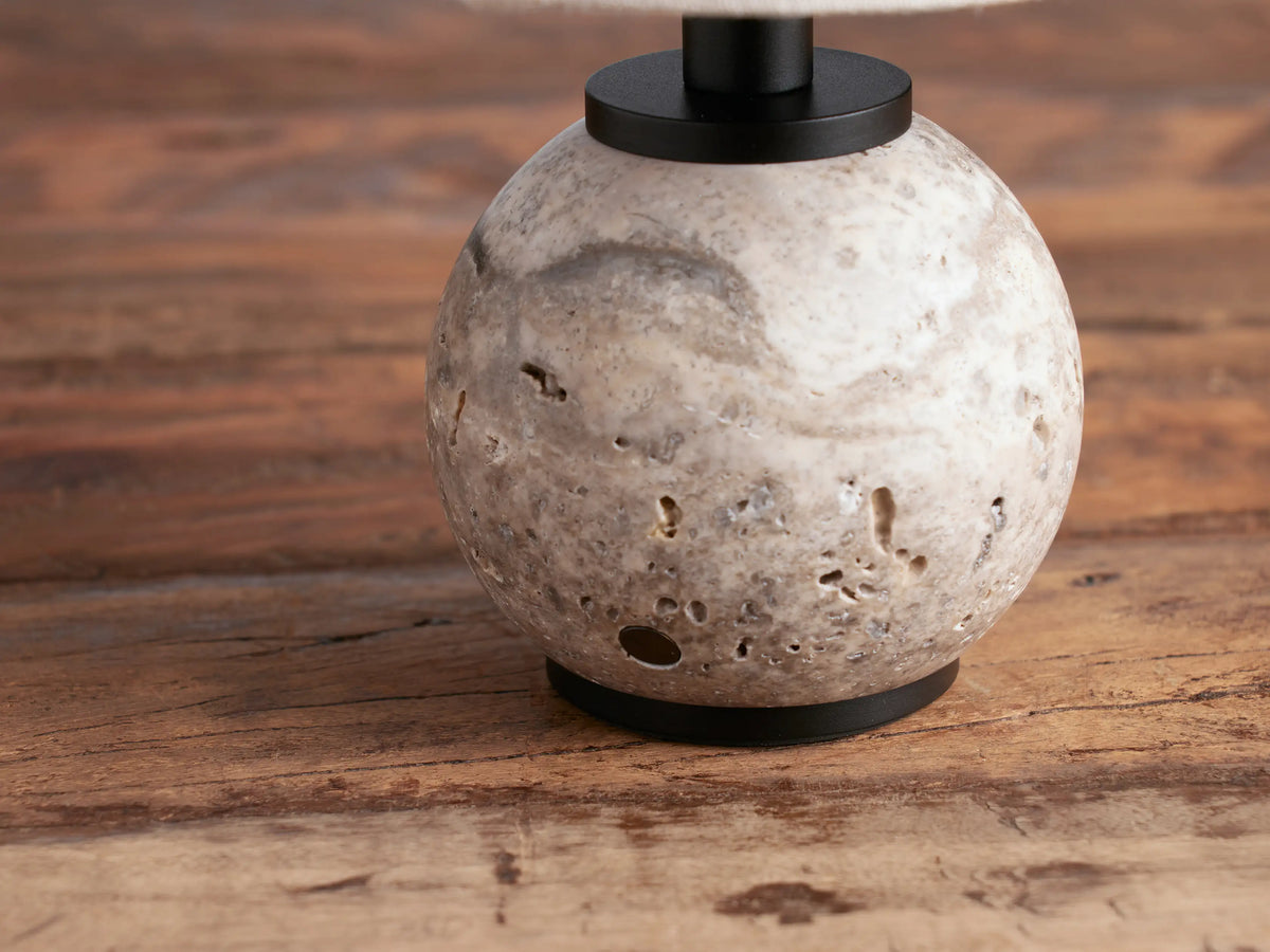 Celia Outdoor Rechargeable Lamp with a round grey textured stone base, black hardware, and flax linen conical shade on a wooden table.