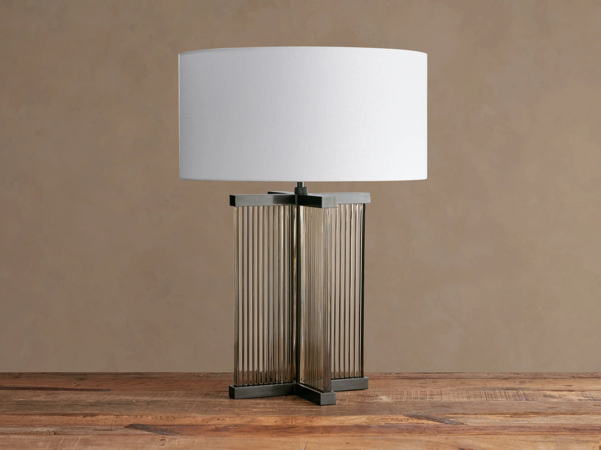 Delsie Table Lamp with an off-white shade, clear fluted glass base with dark bronze framing, on a rustic wood table.