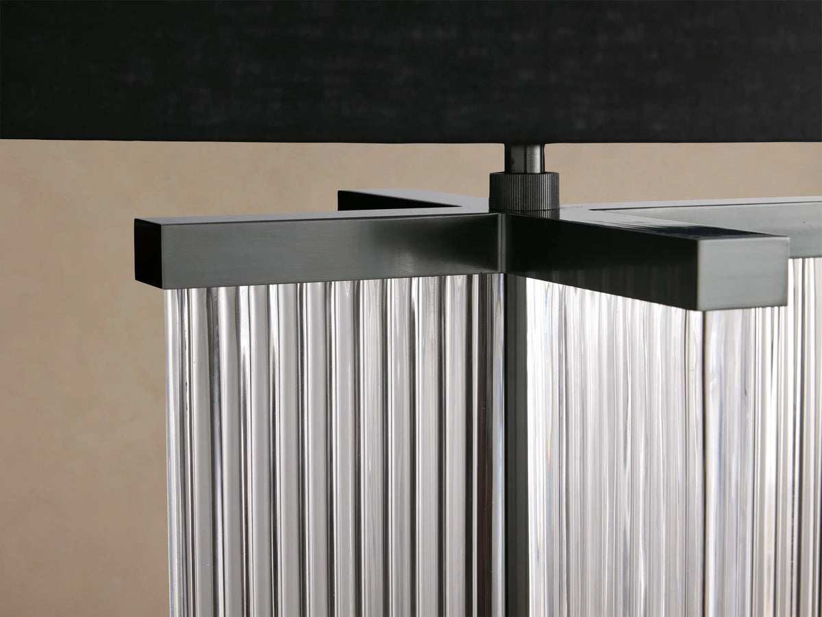 Delsie Table Lamp with a black cylindrical shade, a fluted clear glass column base, and dark bronze accents on a wood table.