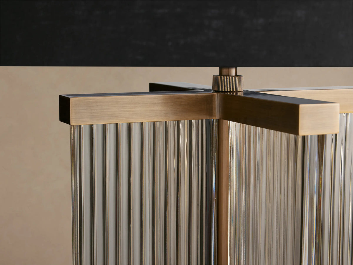 Delsie Table Lamp with black drum shade, burnished brass base, and clear fluted glass columns on a wooden surface.