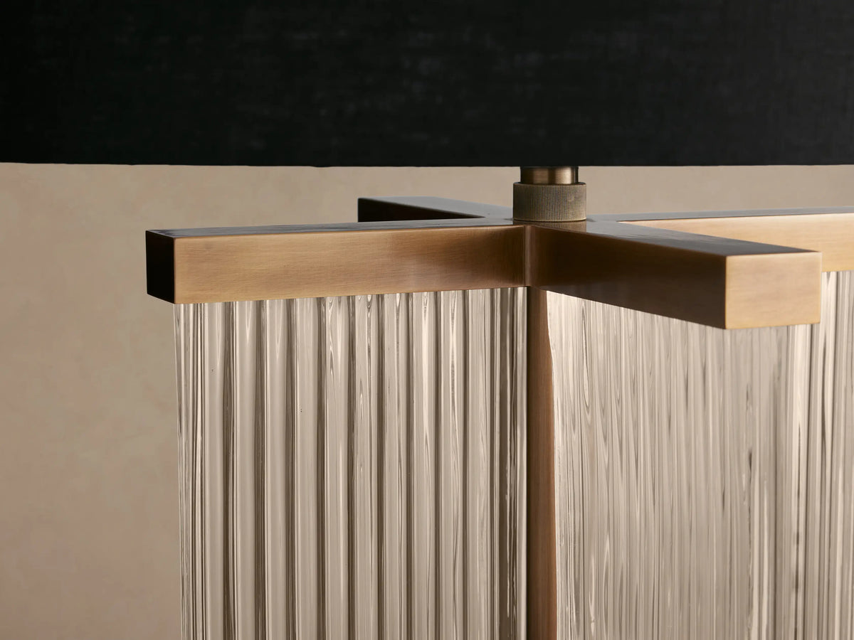 Delsie Table Lamp: black cylindrical shade, fluted glass body with burnished brass accents, on a rustic wooden table.