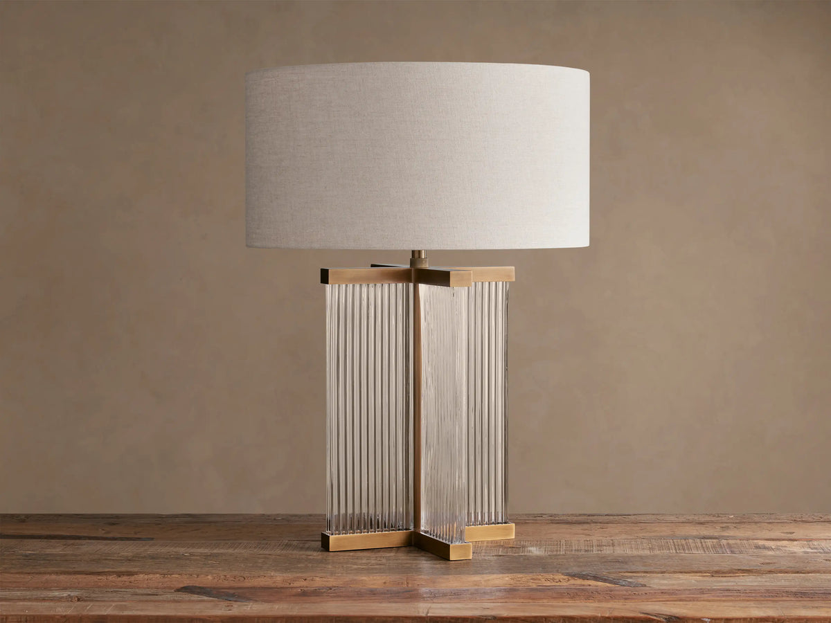Delsie Table Lamp with flax linen shade, fluted glass base, and burnished brass accents on a rustic wooden surface.