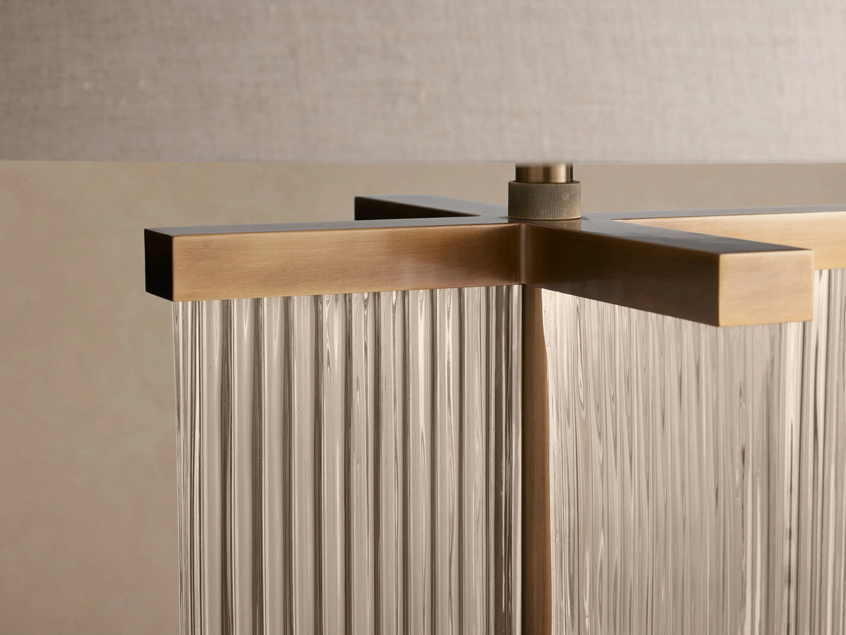 Delsie Table Lamp with clear fluted glass and burnished brass base, topped with a light-colored cylindrical shade on a wooden table.