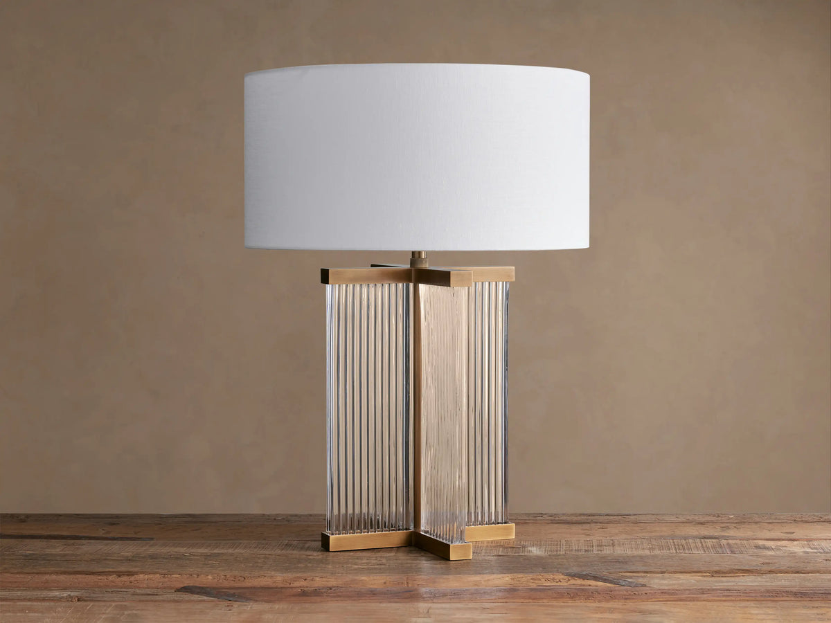 Delsie Table Lamp with white drum shade, fluted glass and burnished brass base on a rustic wooden table.