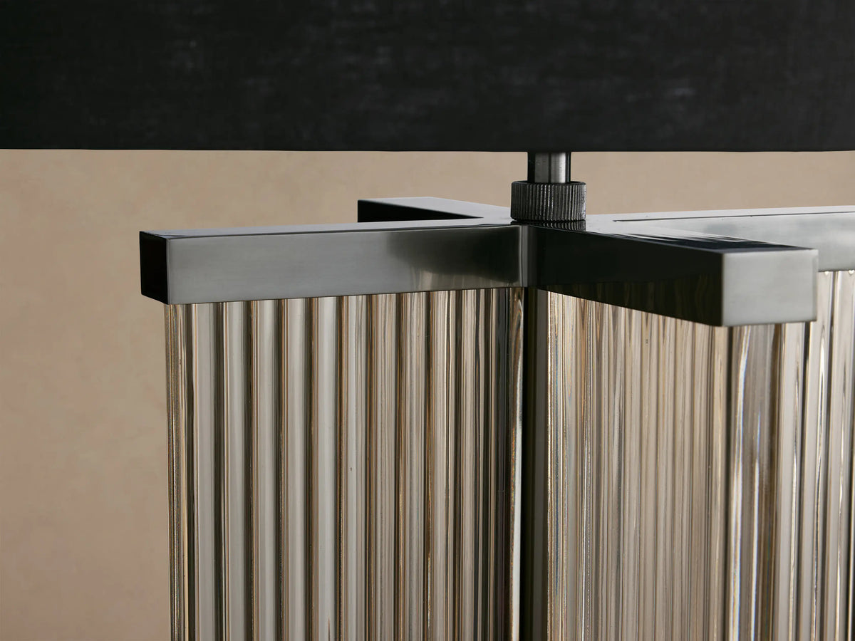 Delsie Table Lamp. Black drum shade atop a fluted glass base with burnished bronze metal, on a rustic wooden table.
