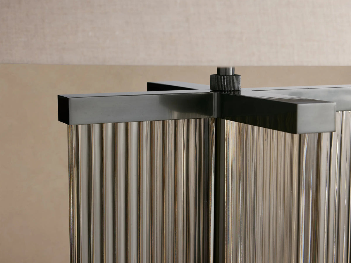Delsie Table Lamp with light flax drum shade, bronze finish steel, and fluted glass base on a wooden table.