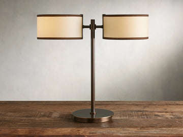 Daphne 2-Light Table Lamp with bronze-finished steel base and two cream shades with brown trim on a wooden surface.