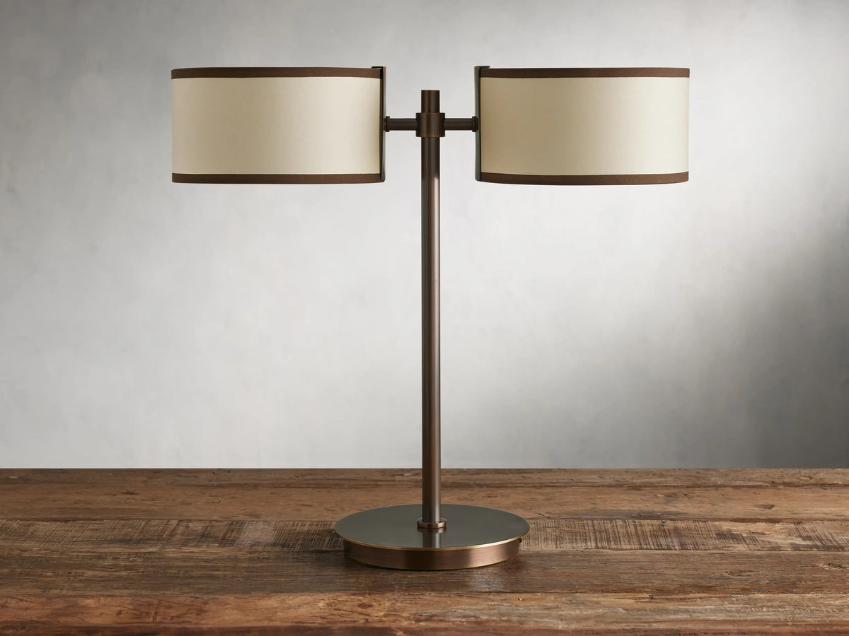 Daphne 2-Light Table Lamp with bronze-finished steel base and two cream shades with brown trim on a wooden surface.