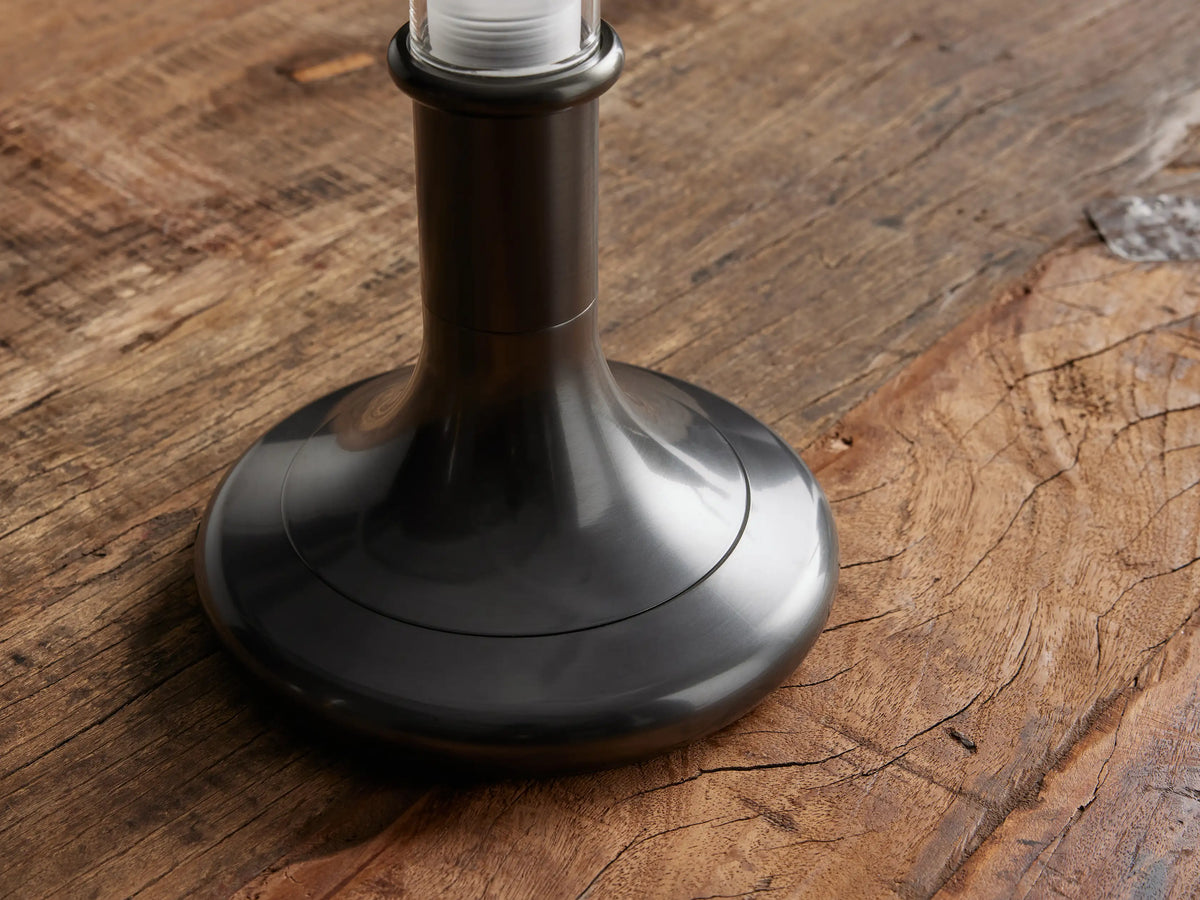 Luella Outdoor Rechargeable Lamp with a slender glass cylinder atop a brushed bronze base on a wooden surface.