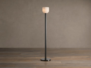 Ansley Floor Lamp: tall, dark steel pole and round base with an illuminated natural alabaster stone shade on a wooden floor.