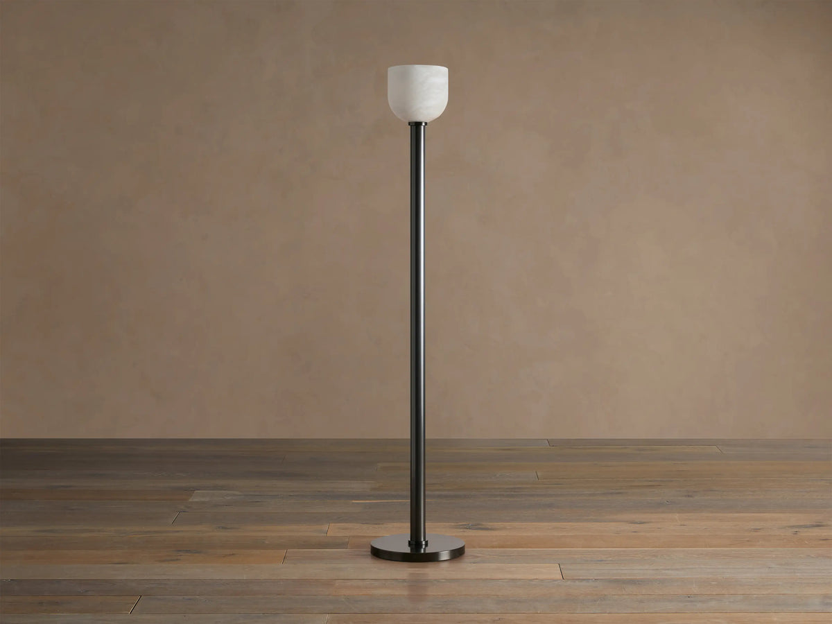 Ansley Floor Lamp: tall, dark steel pole and round base with an illuminated natural alabaster stone shade on a wooden floor.