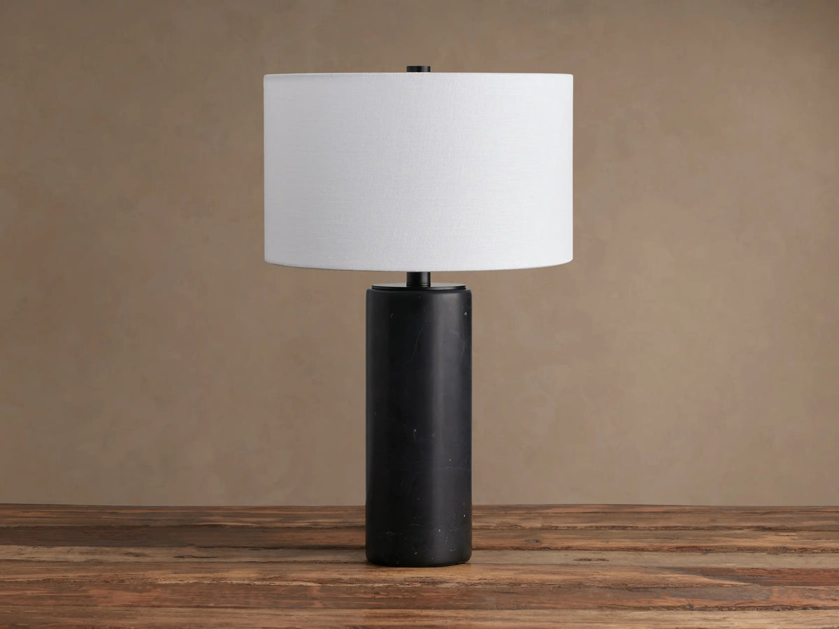 Brixton Table Lamp featuring a dark cylindrical marble base, short dark metal neck, and a white fabric drum shade, on a wooden table.