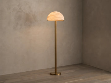 Front view of a brushed brass floor lamp with a half-dome mottled glass shade, emitting a warm glow.