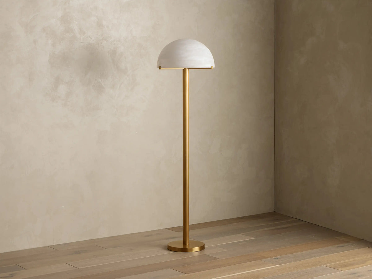 Front view of a brushed brass floor lamp with a half-dome mottled glass shade, emitting a warm glow.