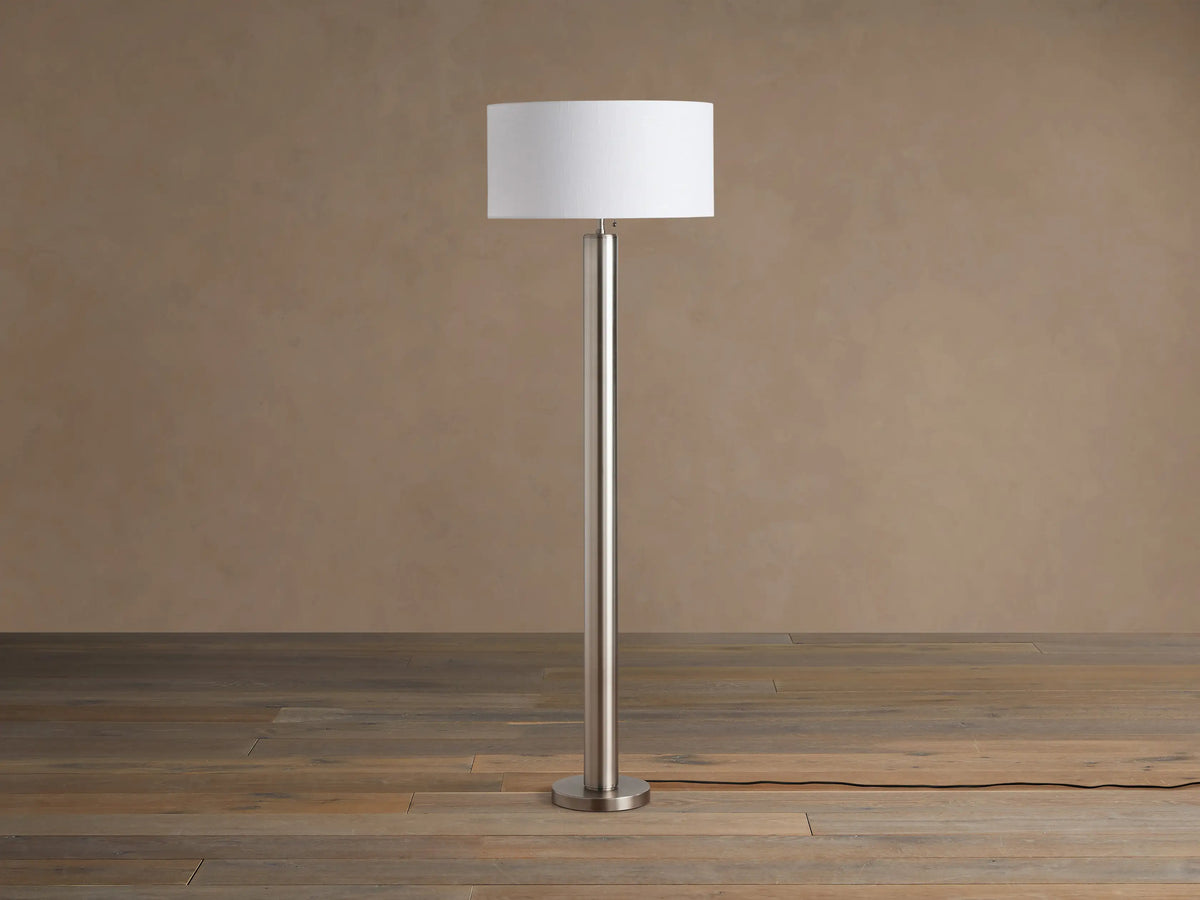 Linden Floor Lamp in Pewter: Tall, slender, metallic pewter finish pole and round base, with a white cylindrical linen shade.