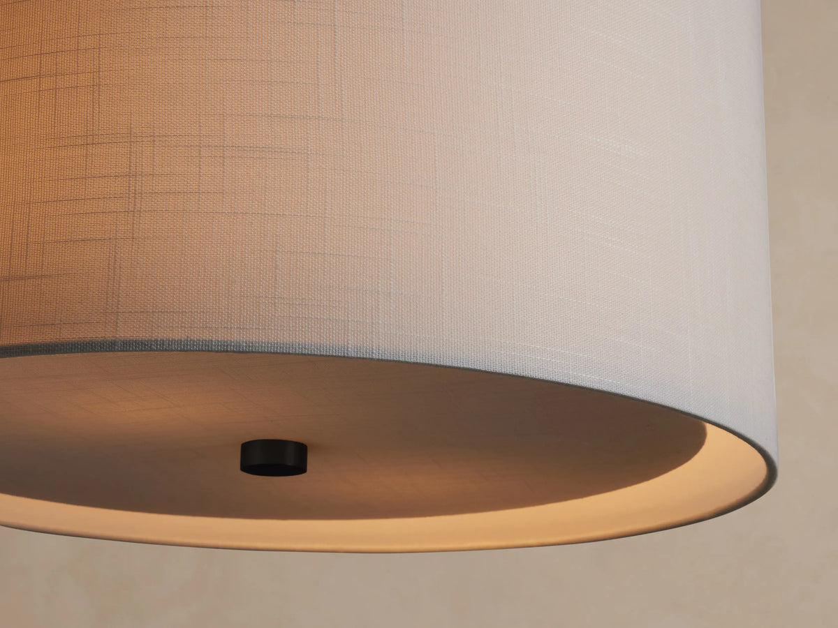 Linden Pendant: Light gray cylindrical linen shade hanging from a dark metal rod against a warm beige wall.