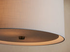 Linden Pendant with a light gray textured linen drum shade and brushed nickel hardware, hanging against a beige wall.