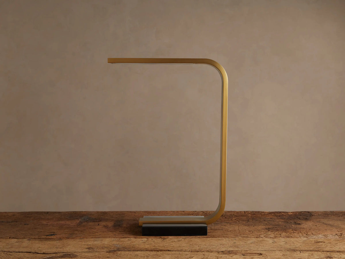 Karson Task Table Lamp: sleek brass, U-shaped lamp with an illuminated LED strip, on a black marble base, resting on a wooden table.