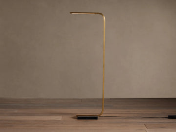 Modern brass Karson Task Floor Lamp with a curved stem, glowing light strip, and black marble base on a wood floor.