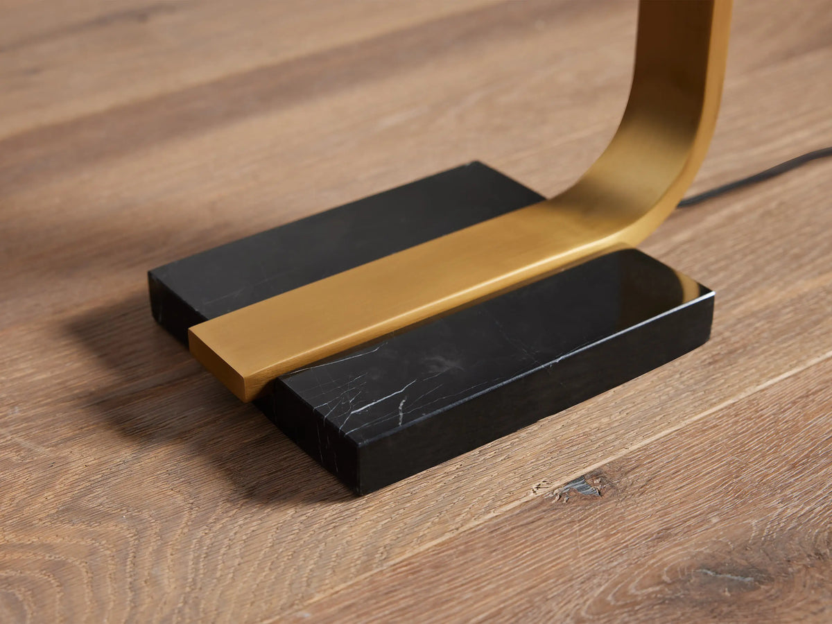 Karson Task Floor Lamp's U-shaped brass arm extending from its two-piece rectangular black marble base on wood flooring.