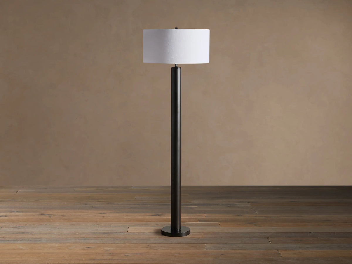 Linden Floor Lamp: tall, dark bronze-finished pole with a round base, topped by an illuminated white cylindrical linen shade.