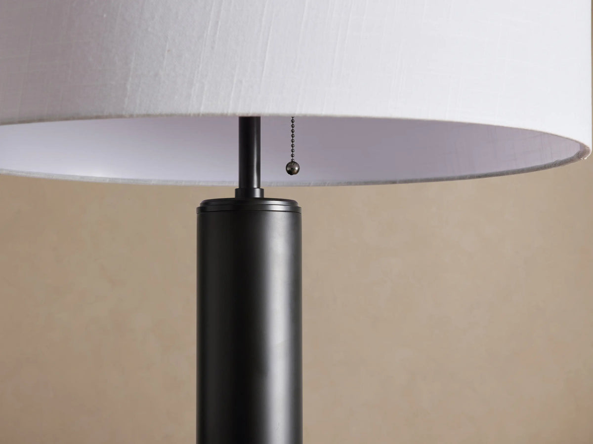 Linden Floor Lamp with a dark bronze iron pole and round base, topped by a white cylindrical linen shade, on a wood floor.