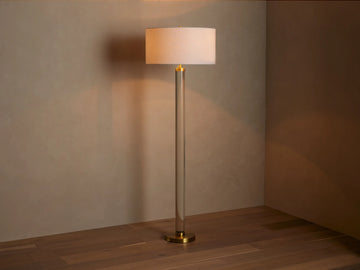 Linden Crystal Floor Lamp with clear column, brass accents, and an illuminated off-white linen shade, on a wood floor.