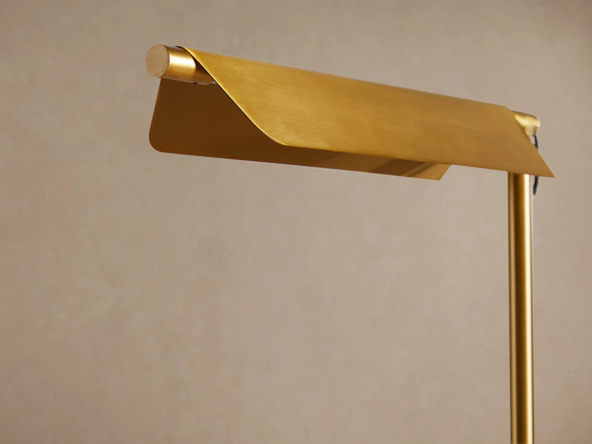 Axle Brass Floor Lamp with a slim brass pole, horizontal rectangular shade, and light square base on a wood floor.