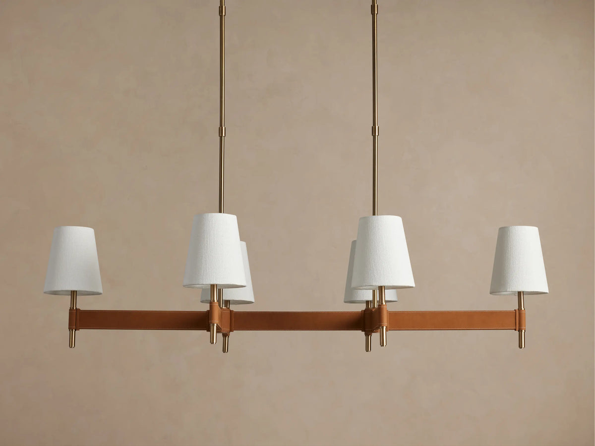 Hastings Linear Chandelier with 6 white linen shades on a brown leather-wrapped bar, suspended by antiqued brass rods.