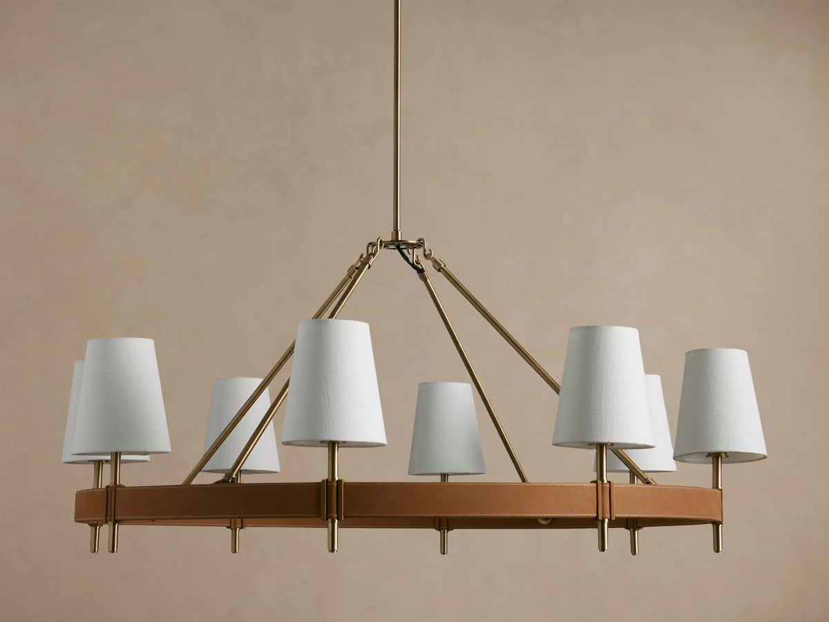Hastings Round Chandelier: round antiqued brass frame with brown leather, 8 illuminated white linen shades.