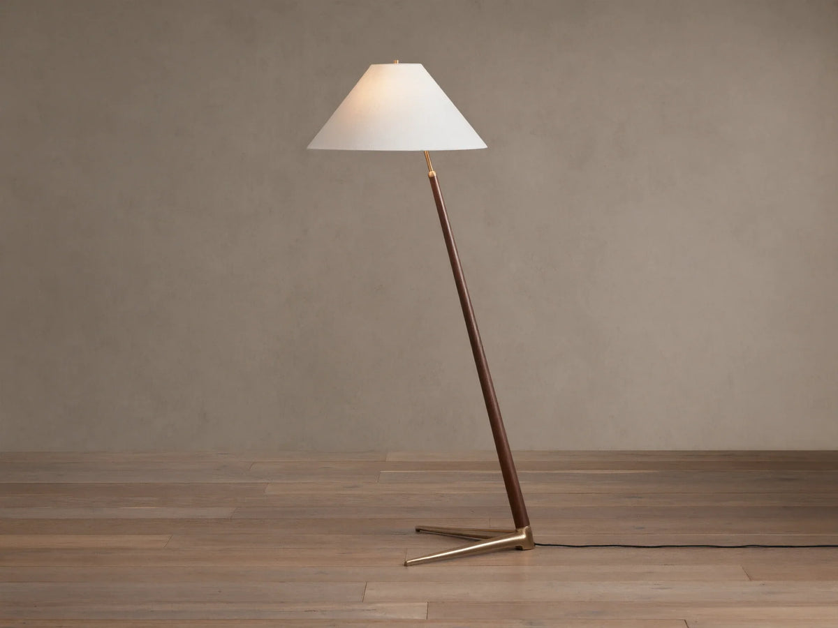 Edric Floor Lamp: Angled walnut wood pole with conical white linen shade and gold brass tripod base on wooden floor.