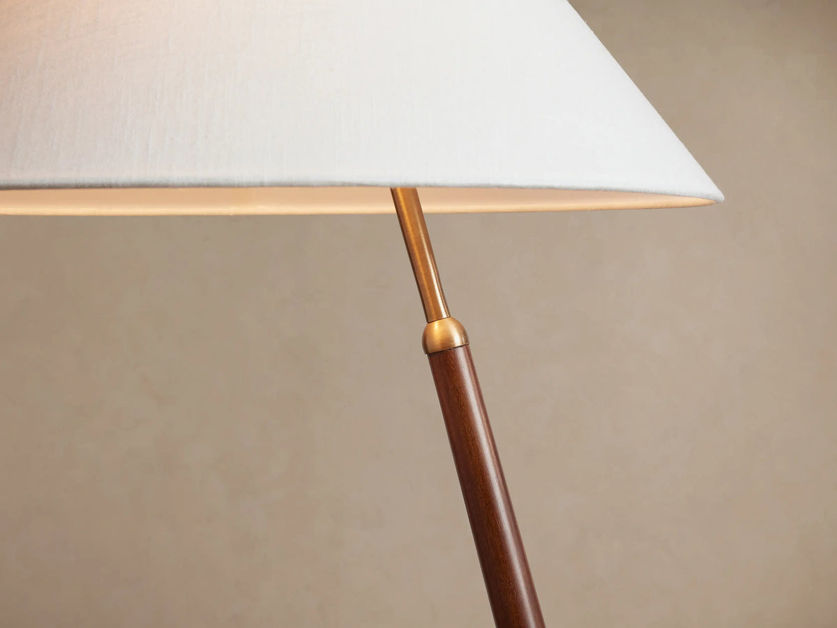 Close-up of Edric Floor Lamp: white linen shade glowing from within, brass arm connecting to a dark walnut wood pole.