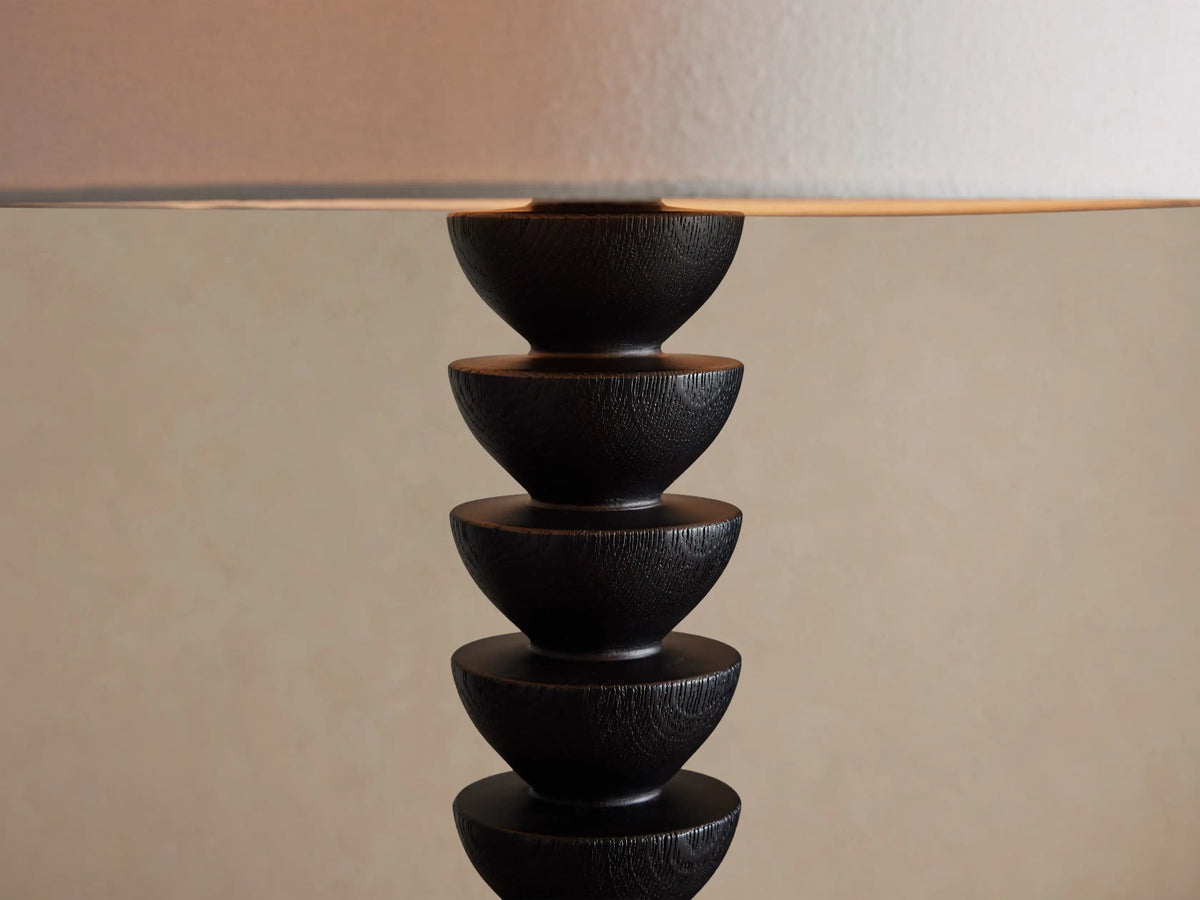 Black Lathe Floor Lamp with white linen shade, featuring a cylindrical base and stacked dark wood disks, on a wooden floor.