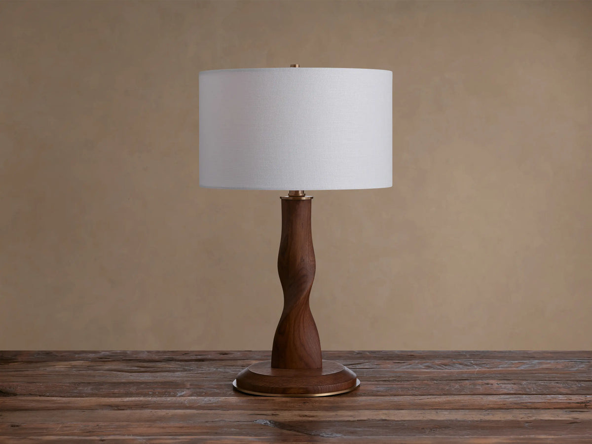 Jonas Table Lamp: Light flax linen shade, dark twisted oak wood stem & base, brass accents, on a rustic wood surface.