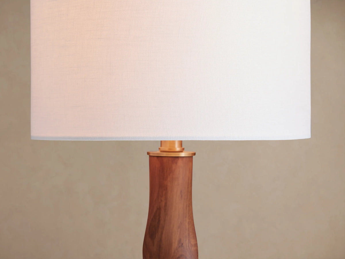 Jonas Table Lamp with a white linen shade and a twisted dark oak wood base with brass accents, on a rustic wooden table.