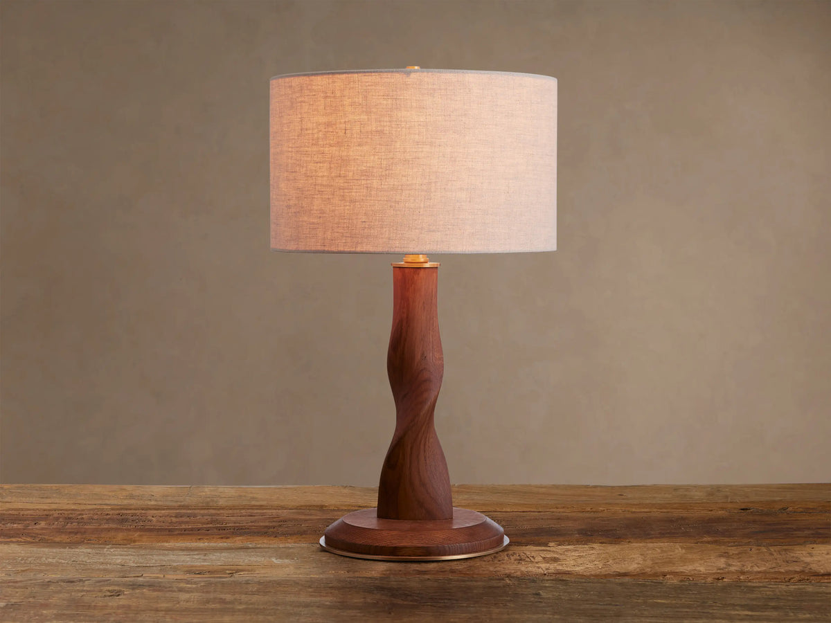 Jonas Table Lamp with a light flax linen shade, twisted dark oak wood base, and brass accents, sitting on a rustic wooden table.