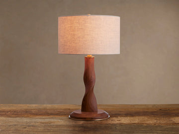 Jonas Table Lamp with a light flax linen shade, twisted dark oak wood base, and brass accents, sitting on a rustic wooden table.