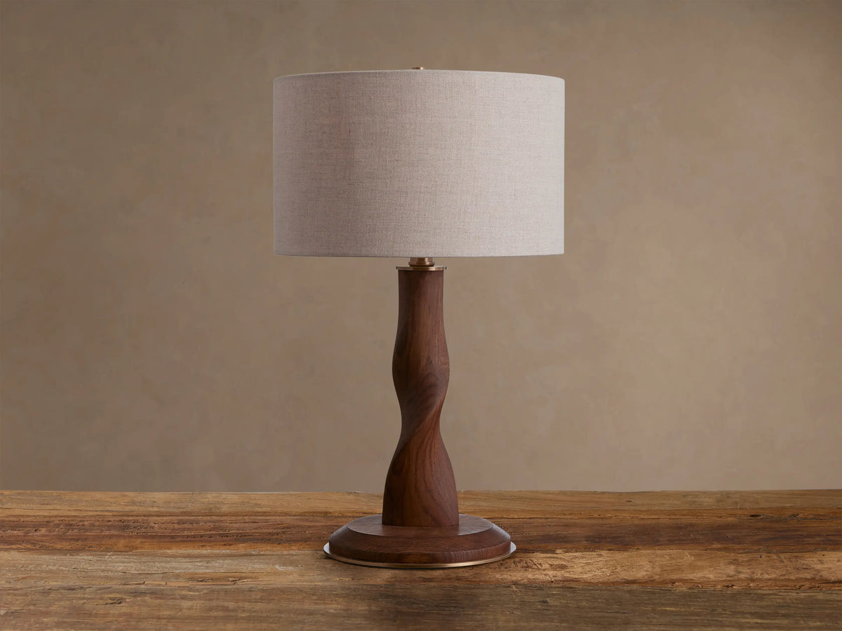 Jonas Table Lamp with a light flax linen shade, twisted dark oak wood base, and brass accents, sitting on a rustic wooden table.