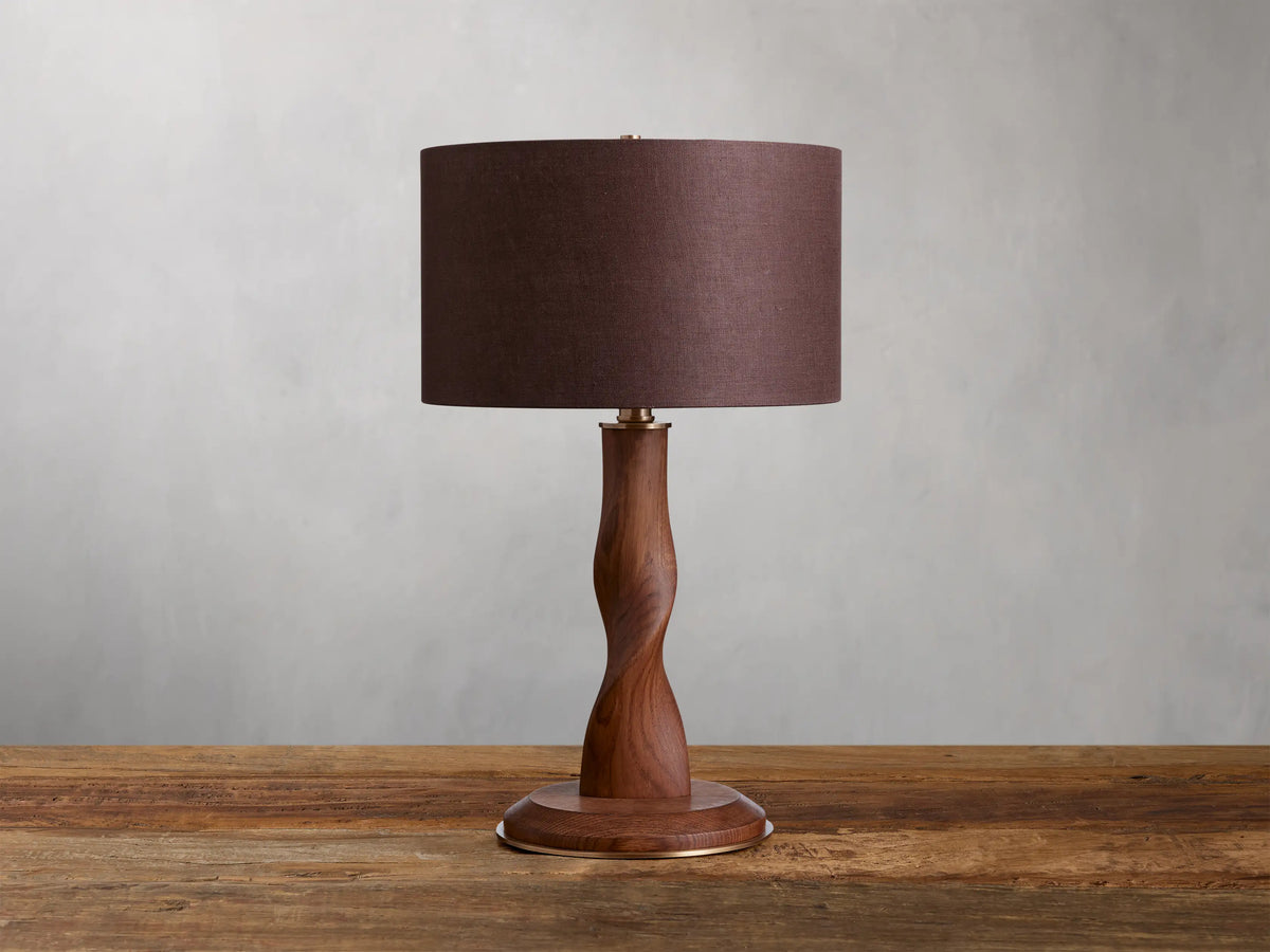 Jonas Table Lamp on a wooden surface; oak wood base with brass accents and a brown linen shade against a neutral background.