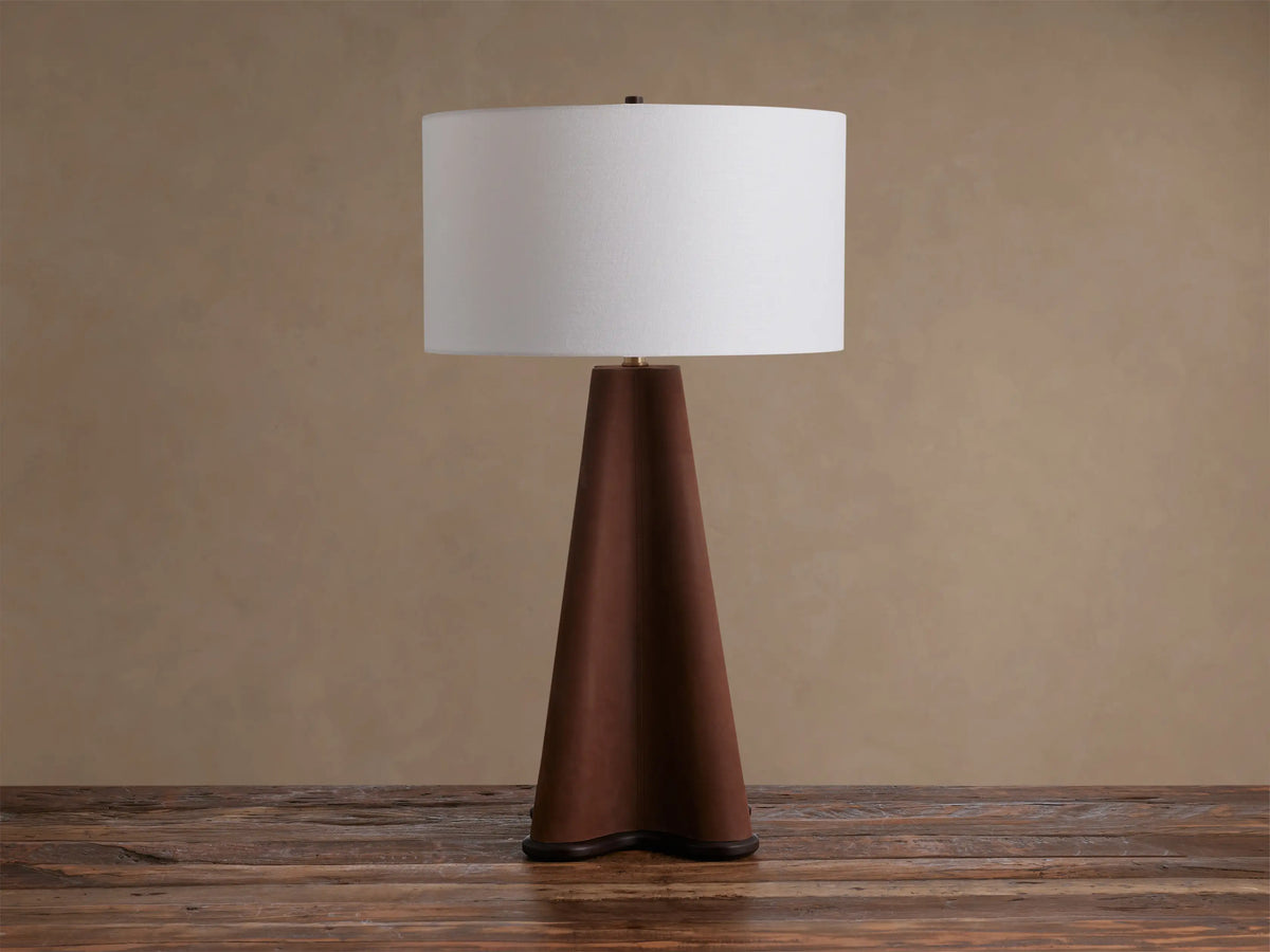 Volant Table Lamp: conical dark oak wood base, brass accent, and cream linen shade, illuminated on a rustic wooden table.