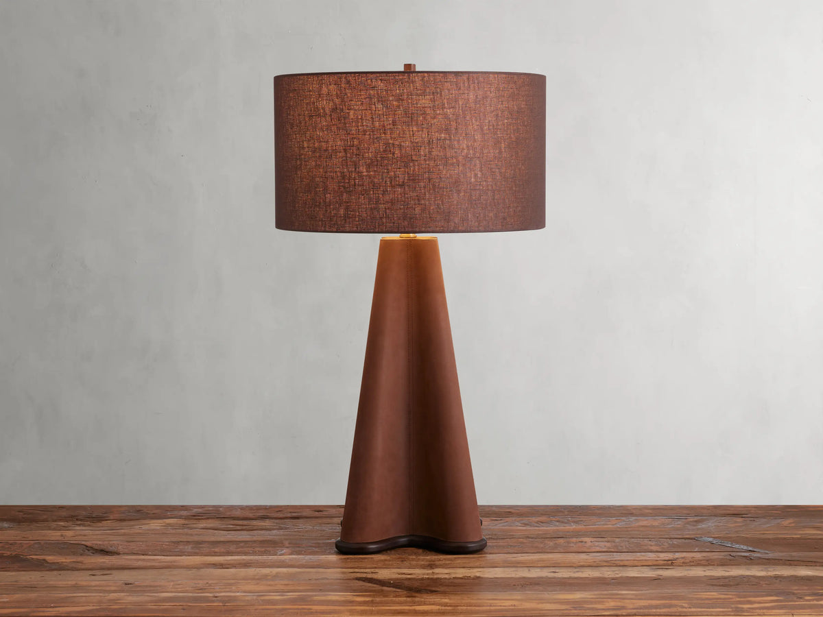Volant Table Lamp with cone-shaped oak wood base, brass accents, and brown linen shade on a wooden surface.