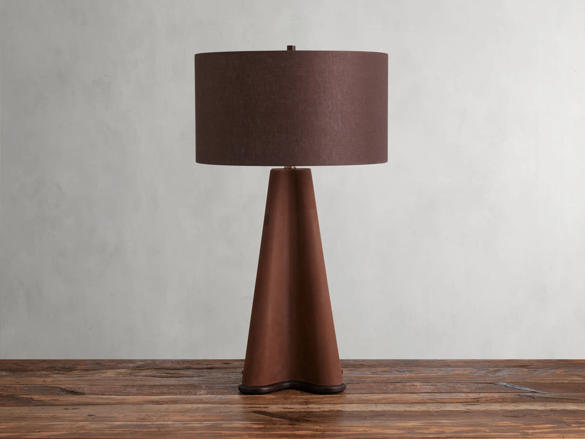 Volant Table Lamp with cone-shaped oak wood base, brass accents, and brown linen shade on a wooden surface.