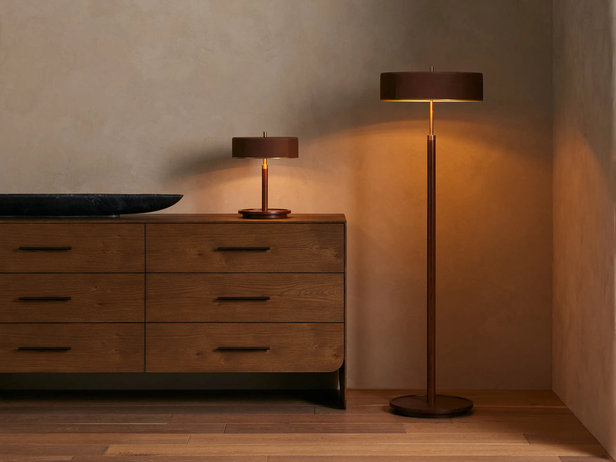A close-up of a lamp showing a brown fabric drum shade with a gold interior. The lamp features a wooden base with a brass accent.
