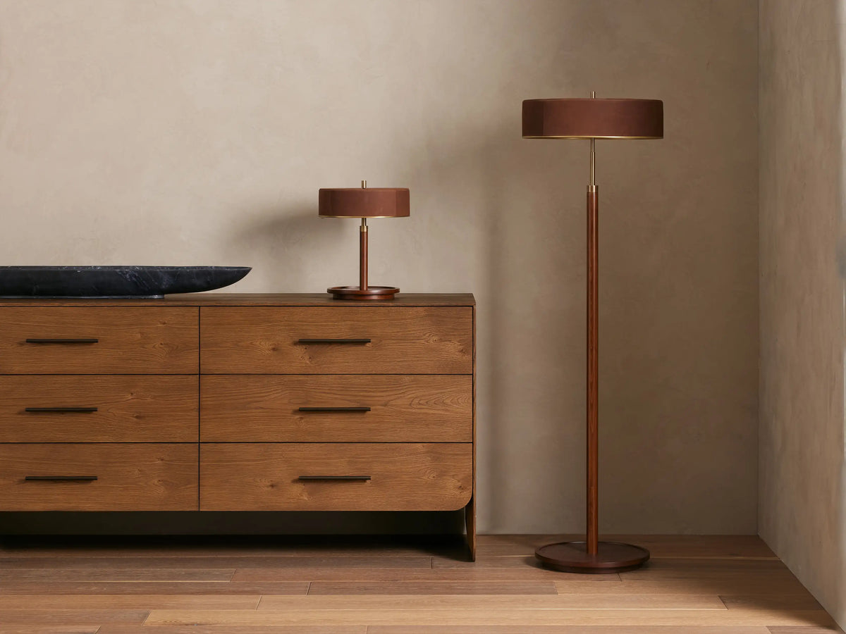 Anakin Table Lamp with a dark brown nubuck leather shade, brass accents, and a dark wooden base, illuminated with a warm glow.