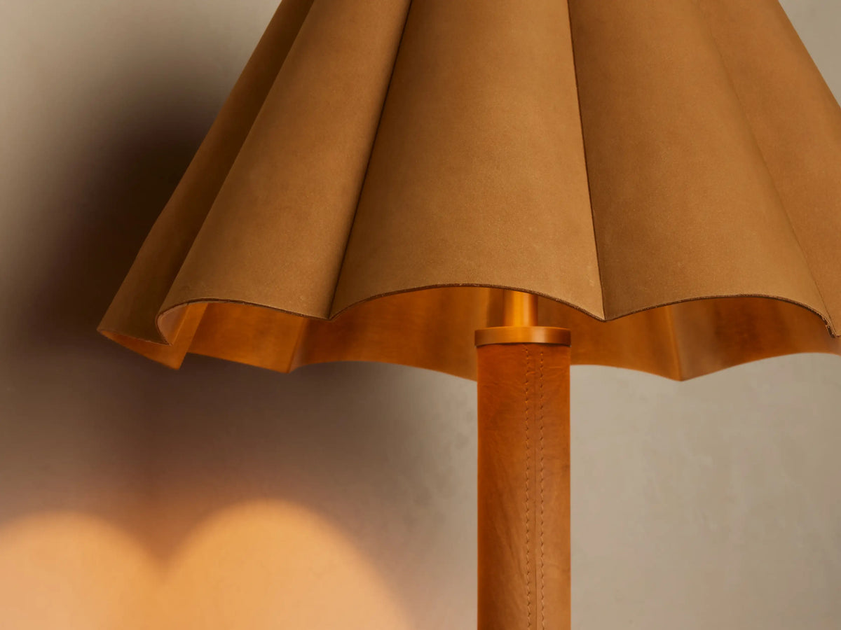 Lucy Accent Table Lamp close-up, showing its pleated brown leather shade with golden interior and stitched leather stem. Warm light cast.