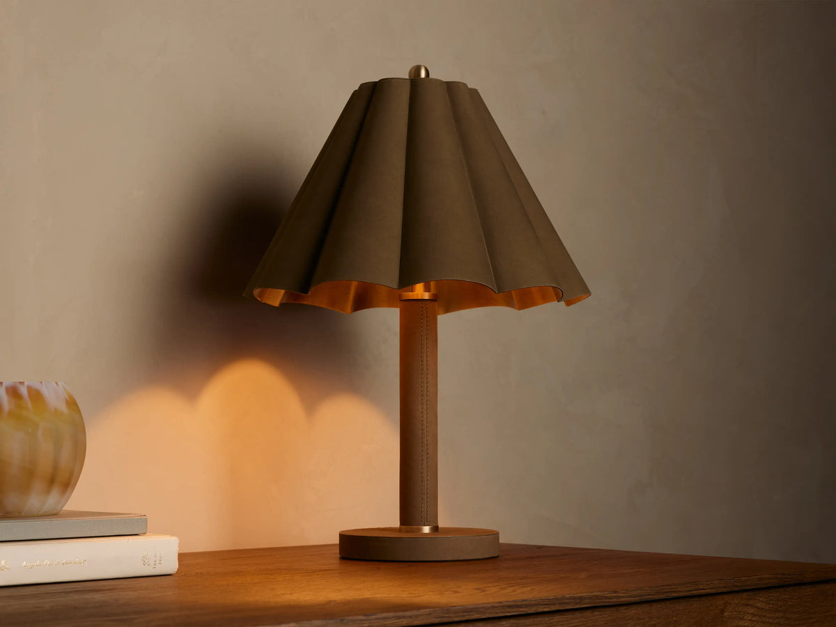 Lucy Accent Table Lamp with pleated dark brown leather shade, gold interior, and tan leather base on a wooden table, emitting a warm glow.
